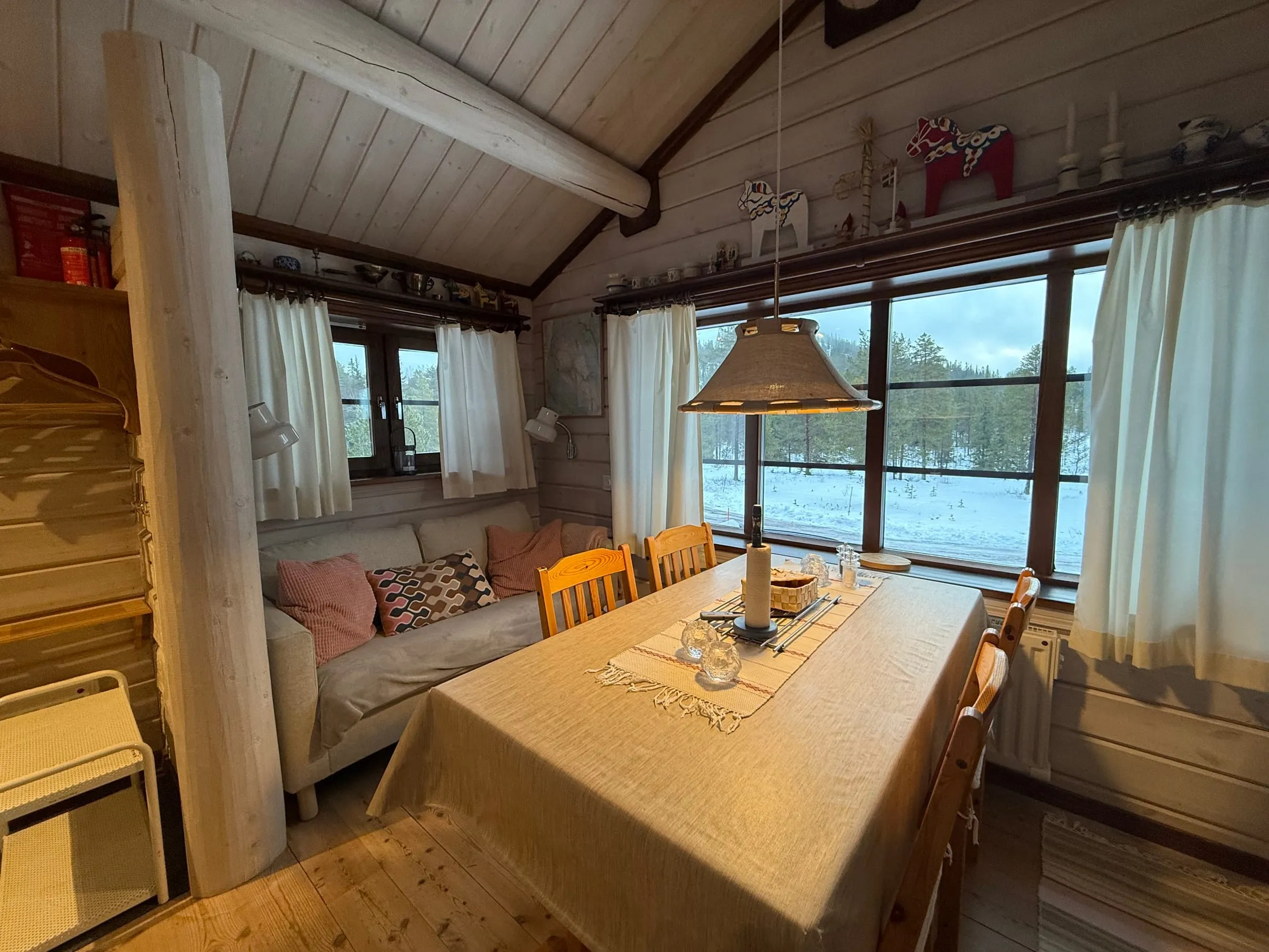 Living room with dining table and sofa. The ceiling is high up with visible beams – which creates a feeling of volume.