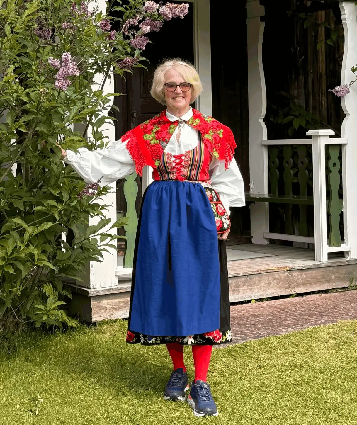 Kerstin Rise i folkdräkt framför en farstukvist med syrener